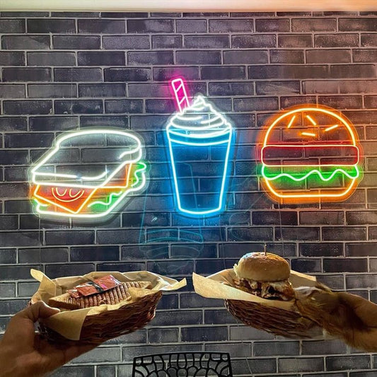 Sandwich Shake Burger Neon Sign | Custom Neon Sign | Neon for Restaurants Neon signs of a burger, cup, and sandwich on a brick wall with hands holding food below.