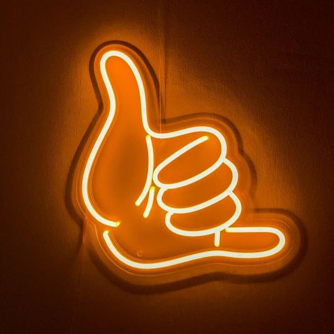 Shaka Hand Neon Sign | Custom Neon Sign | Neon for Living Room Decor Neon sign shaped like a hand giving a thumbs up on a brown background