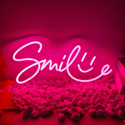 Smile Neon Sign | Custom Neon Sign | Neon for Living Room Decor Neon sign with 'Smile' on a pink background with plush toys.
