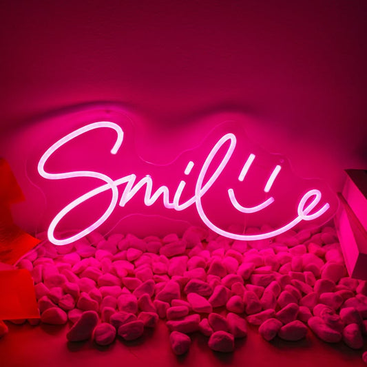 Smile Neon Sign | Custom Neon Sign | Neon for Living Room Decor Neon sign with 'Smile' on a pink background with plush toys.