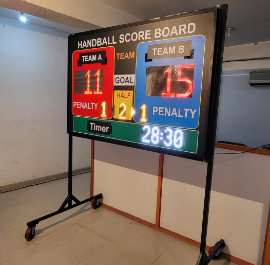 The Seven Colours LED Sports Scoreboard | LED Running Sports Scoreboard for Cricket | Led Cricket Scoreboard for Football, Volleyball, Hockey, Basketball, Badminton, Tennis Handball score board with digital display in a room setting