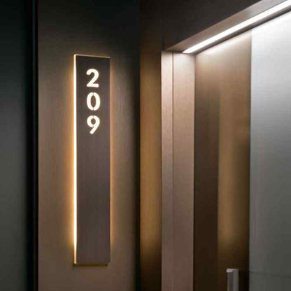 Slim vertical illuminated address plaque displaying house number 209 on a dark panel beside a contemporary wooden entrance door.