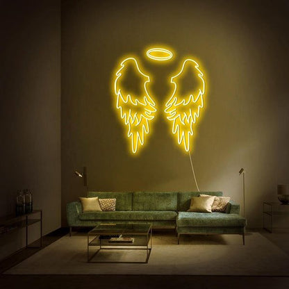 Yellow Wings Neon Sign | Custom Neon Sign | Neon for Living Room Neon angel wings light fixture on a wall above a green sofa in a dimly lit room.