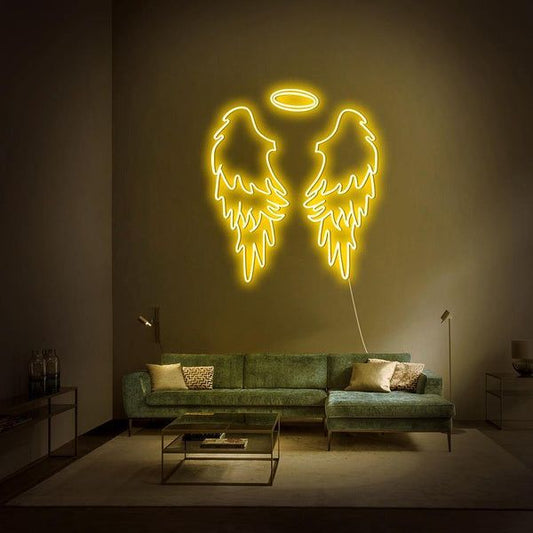 Yellow Wings Neon Sign | Custom Neon Sign | Neon for Living Room Neon angel wings light fixture on a wall above a green sofa in a dimly lit room.