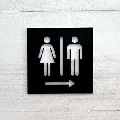 Black restroom direction sign with male female cutout icons and right arrow

