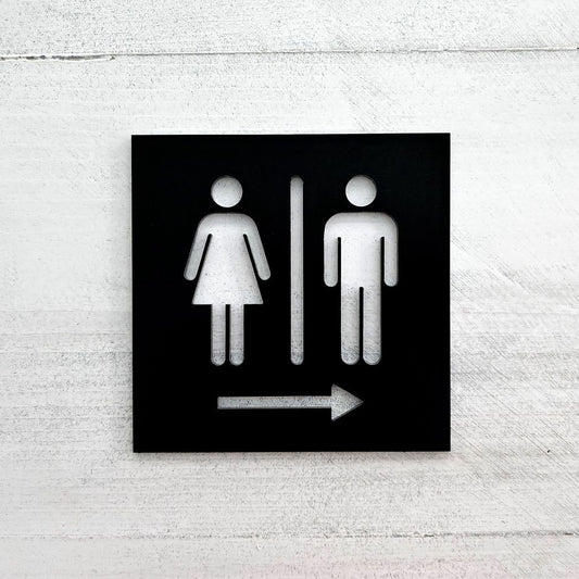 Black restroom direction sign with male female cutout icons and right arrow
