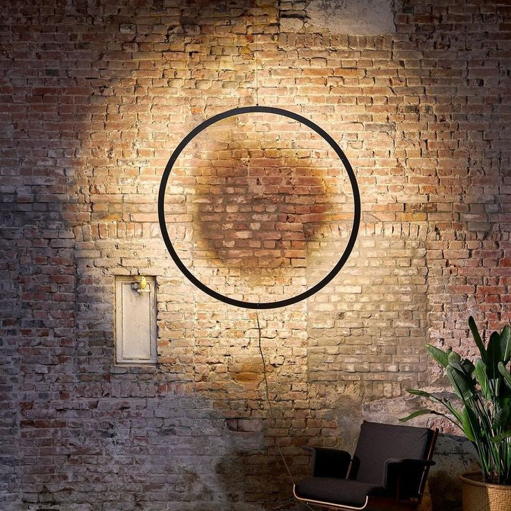 Industrial circular LED ring light with halo wall illumination for modern interiors.