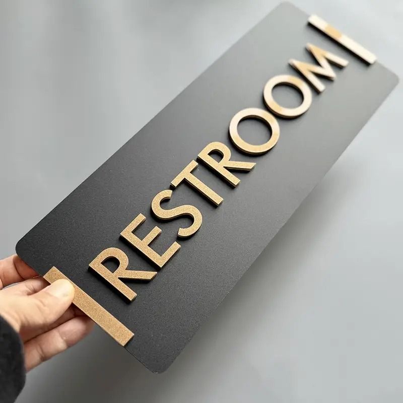 Modern restroom sign board in black with gold lettering

