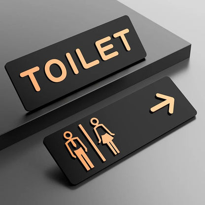 Black and gold toilet direction sign with male female icons and arrow
